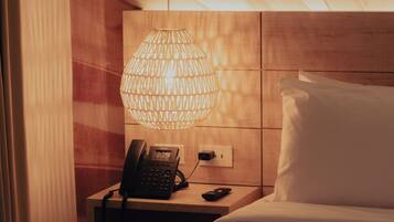 Una habitación de hotel con una cama, una mesita de noche con teléfono, una lámpara y una pared de madera.