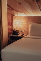 Una habitación de hotel con una cama, una mesita de noche con teléfono, una lámpara y una pared de madera.