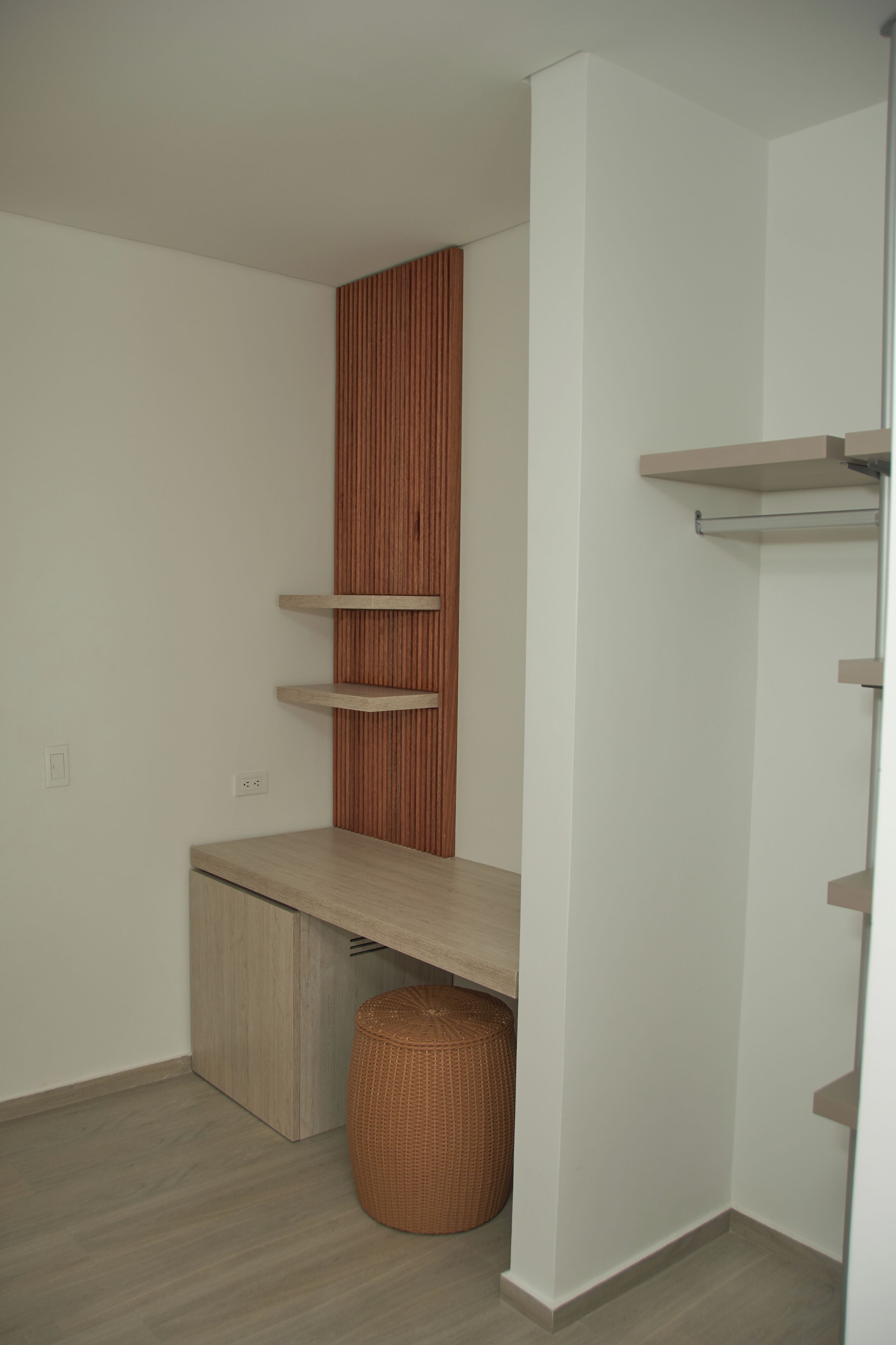 A room with a built-in wooden shelf unit, a small wooden desk, and a wicker basket.