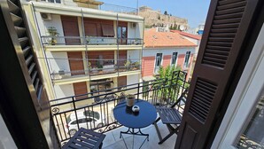 A balcony with a table and chairs, overlooking a cityscape with buildings and a historical monument. - Acropolis Eternal Mansion by YHA  (Athens)