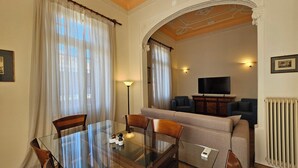 A dining area with a glass table and chairs, a sofa, a television, and a radiator. - Acropolis Eternal Mansion by YHA  (Athens)