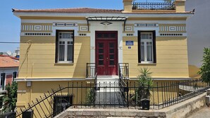 A two-story building with a red door, a balcony with a railing, and a small garden area with potted plants. - Acropolis Eternal Mansion by YHA  (Athens)