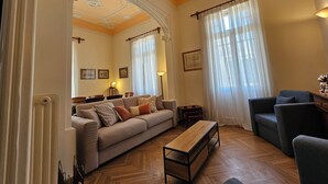 A spacious living room with a sofa, armchairs, a wooden coffee table, and a herringbone-patterned floor. - Acropolis Eternal Mansion by YHA  (Athens)