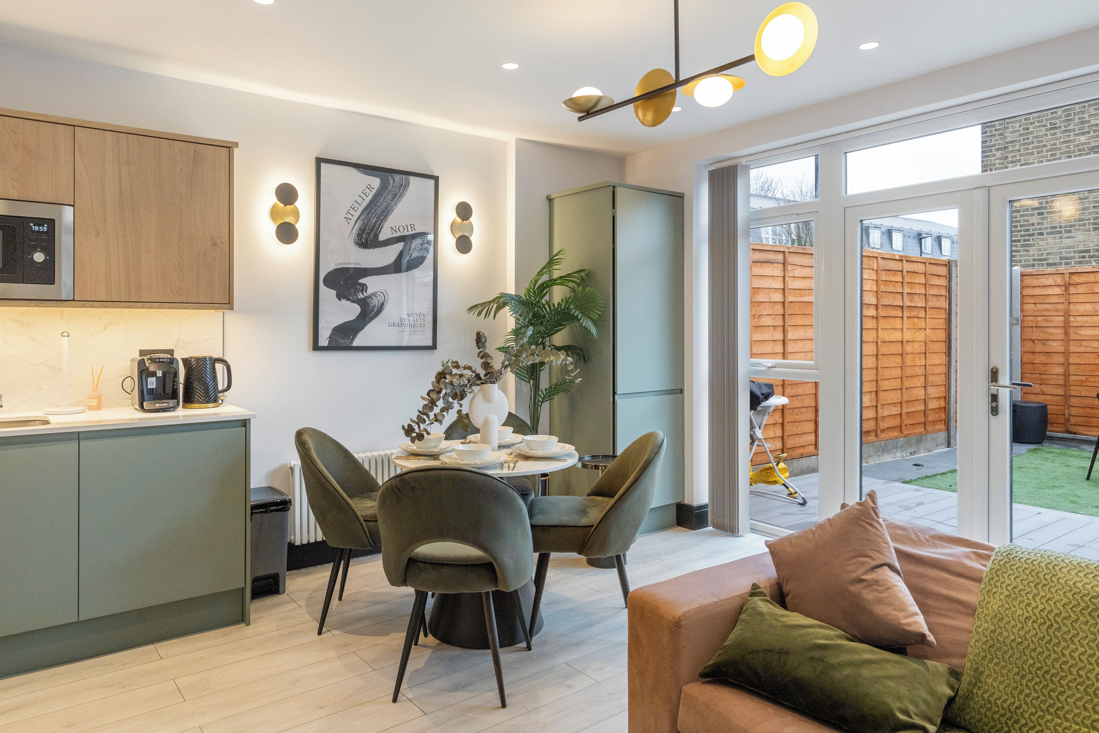 A modern kitchen with a dining area, a sofa, and a view of the backyard.
