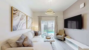 A modern living room with a sofa, armchair, and a flat-screen TV mounted on the wall. - Spacious 4BR+Den Home w/ Pool, 15 Mins to Disney! (Davenport)