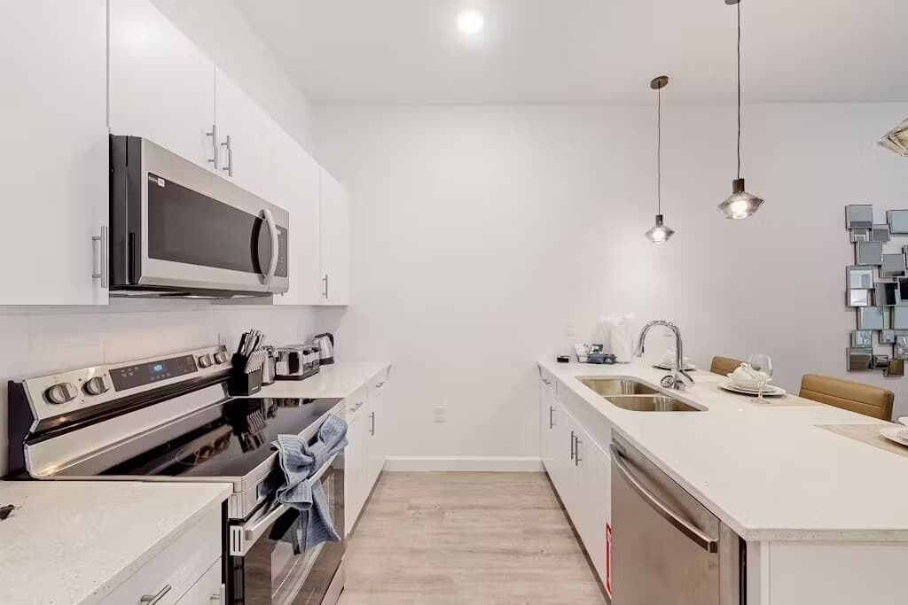 Una cocina moderna con electrodomésticos de acero inoxidable, una isla central con pileta y luminarias colgantes.