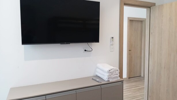 A modern hotel room with a flat-screen TV mounted on the wall, a wooden door, and a small cabinet with towels. - Blue Villas  (Santa Elena)