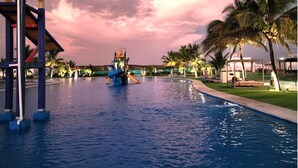 A swimming pool with a water slide and play structures, surrounded by palm trees and a sunset sky. - Blue Villas  (Santa Elena)