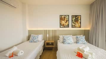 A hotel room with two beds, each with a pillow and a rolled towel. There is a wall-mounted air conditioner and two framed pictures above the beds.