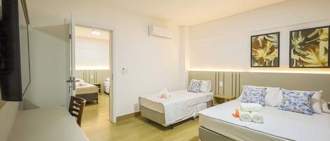 A hotel room with two beds, a desk, a chair, a TV, and artwork on the wall.