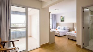 A hotel room with a sliding glass door to a balcony, two beds, a wooden chair, and a shower area. - Tri Hotel Praia Grande (Praia Grande)