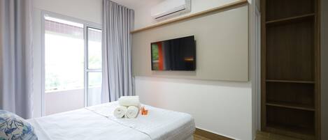Une chambre d’hôtel avec un lit, un téléviseur fixé au mur, un appareil de climatisation au-dessus du lit et une armoire en bois.