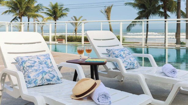 A poolside area with lounge chairs, a table with drinks, and a view of the ocean. - Tri Hotel Praia Grande (Praia Grande)
