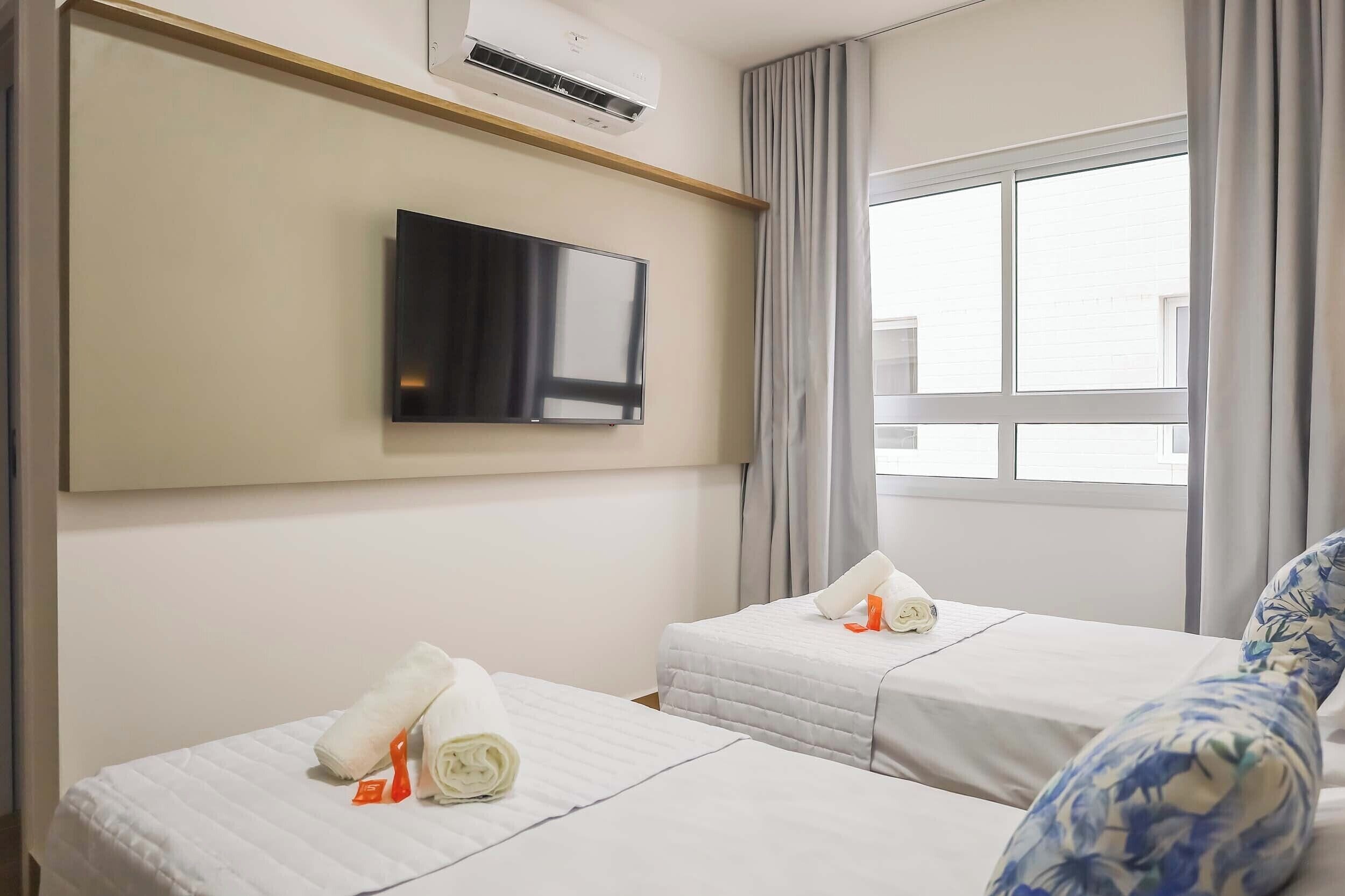 Habitación de hotel con dos camas, un televisor montado en la pared y una ventana con cortinas.