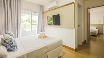 Habitación de hotel con cama, televisor montado en la pared, ventana con cortinas y puerta que da a otra habitación.