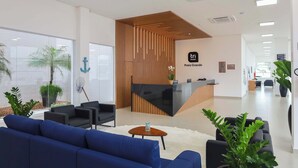 A modern hotel reception area with a wooden reception desk, black sofas, and potted plants. - Tri Hotel Praia Grande (Praia Grande)