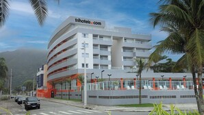 A modern hotel with multiple floors, a prominent website sign, and outdoor seating area. - Tri Hotel Praia Grande (Praia Grande)