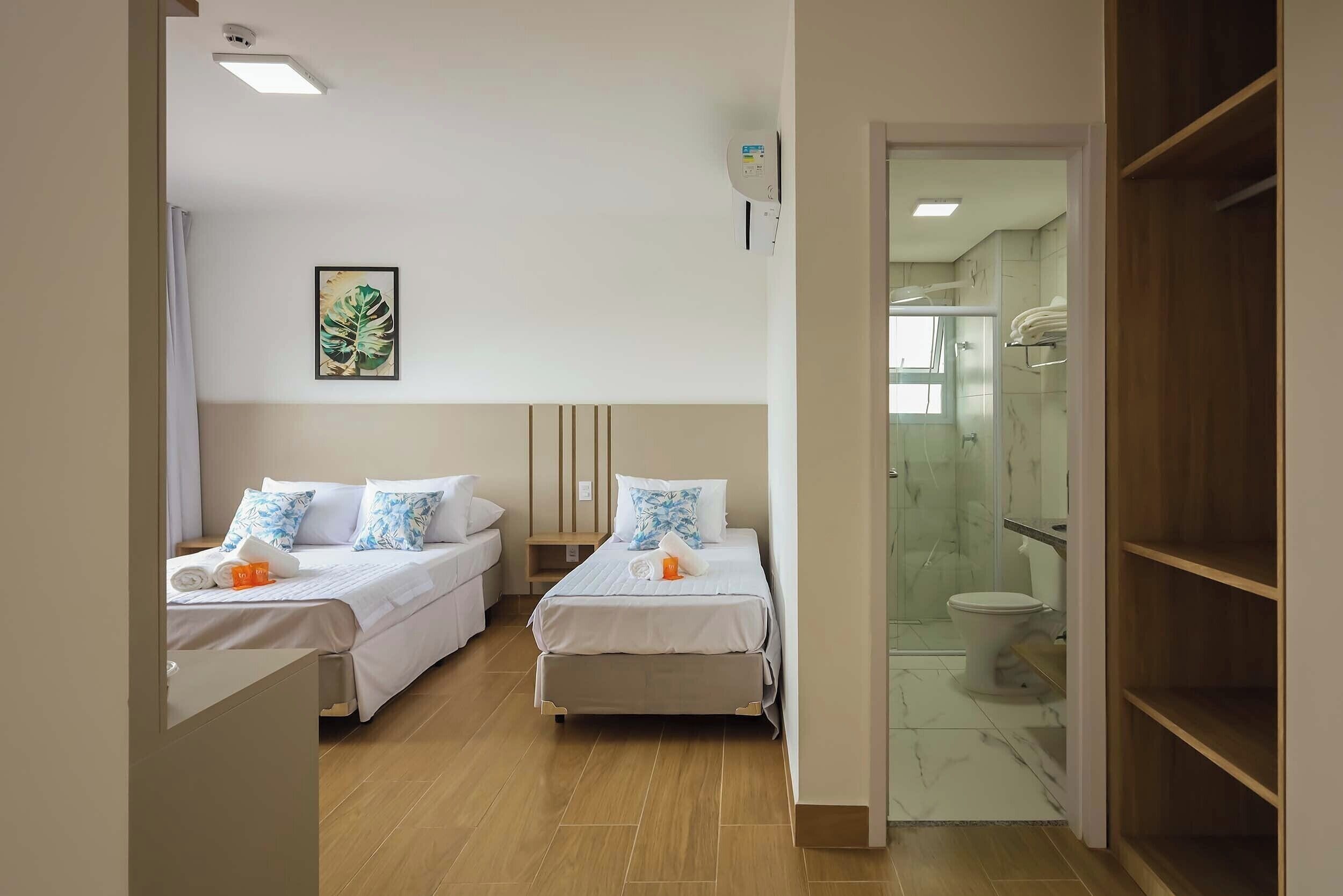 A hotel room with two beds, a bathroom with a glass shower, and a wooden wardrobe.