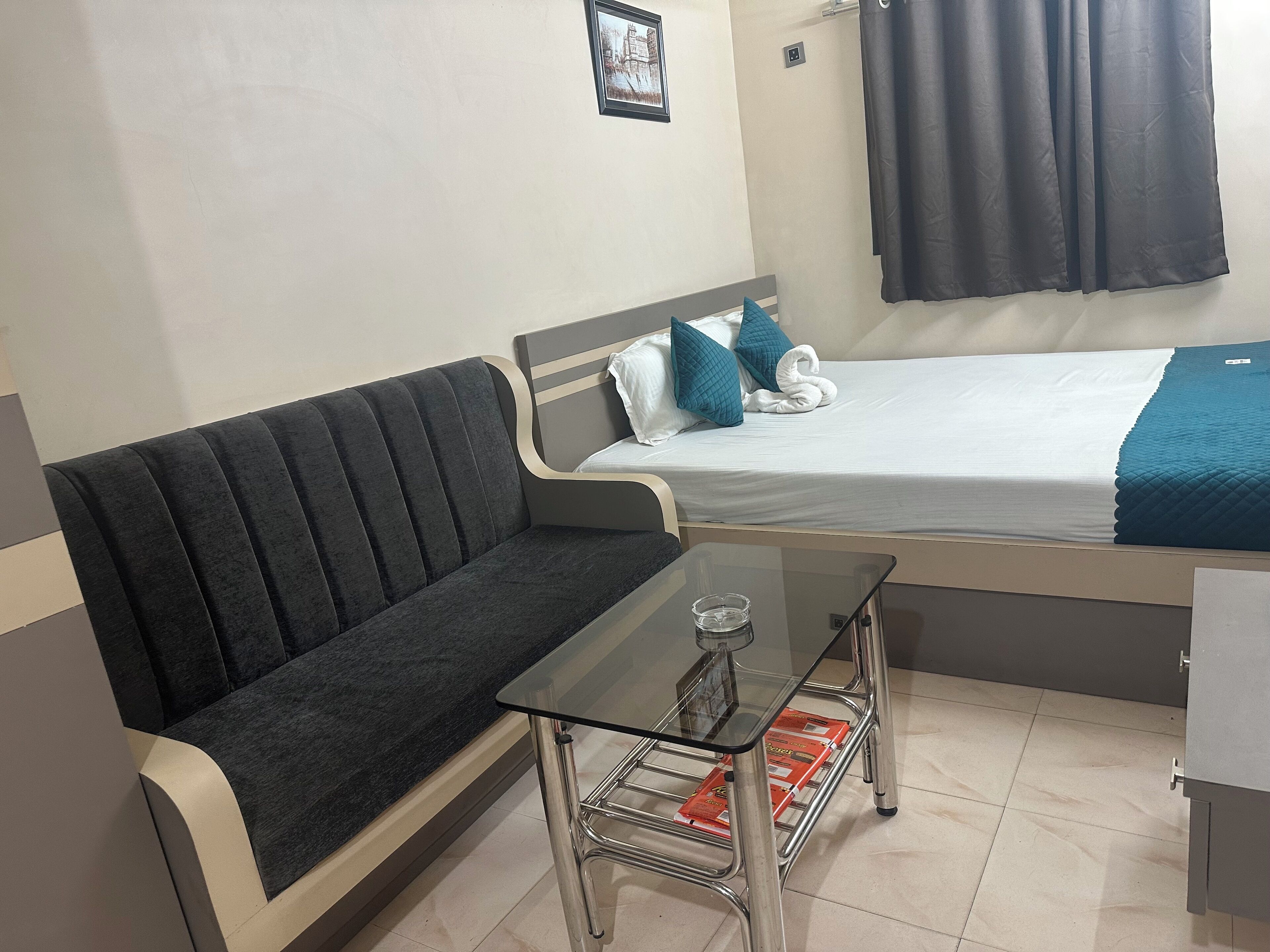 A small, neatly arranged room with a bed, a sofa, and a glass-top table.