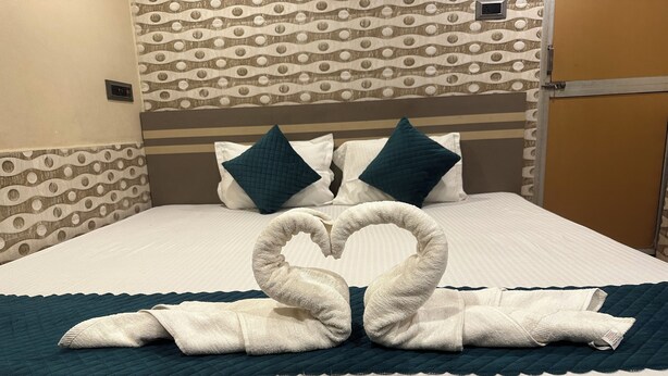 A hotel room with a bed, a heart-shaped towel arrangement, and patterned wallpaper.