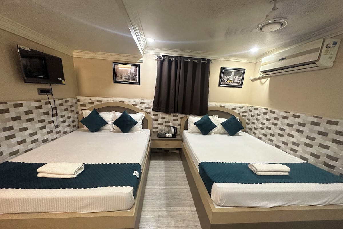 Habitación de hotel con dos camas individuales, un televisor montado en la pared y un equipo de aire acondicionado.