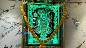A framed religious statue with a garland, set against a marble wall.