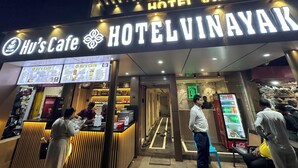 The exterior of Hotel Vinayak with a prominent sign and a coffee shop named Hu's Cafe.