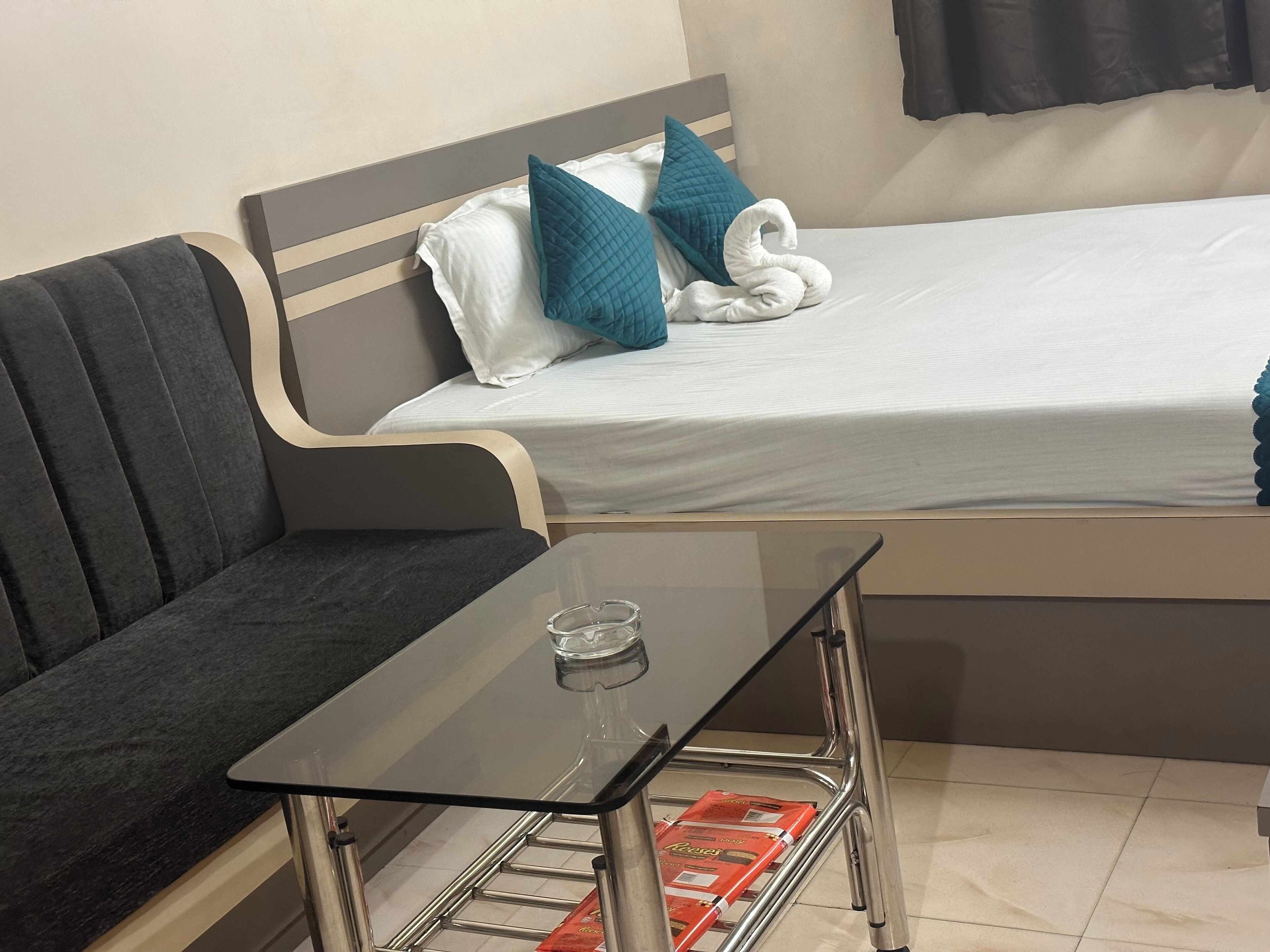 Una habitación de hotel pequeña con una cama, un sofá, una mesa de vidrio y una silla de metal.