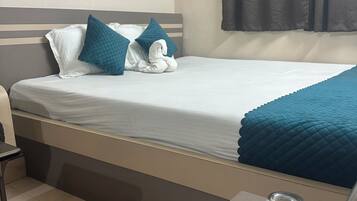 A neatly made bed with a white and teal duvet, a dark curtain, and a framed picture on the wall.