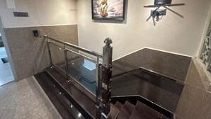 A modern staircase with glass railings, a framed artwork of a ship on the wall, and a small shelf with a device.
