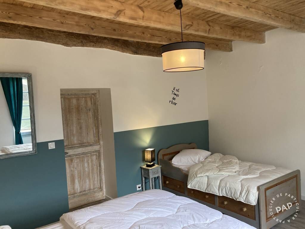 A bedroom with two single beds, a wooden ceiling, a wall-mounted light fixture, and a door with a rustic design.