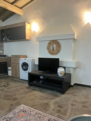 A living room with a flat-screen TV, a washing machine, and a decorative wall piece.