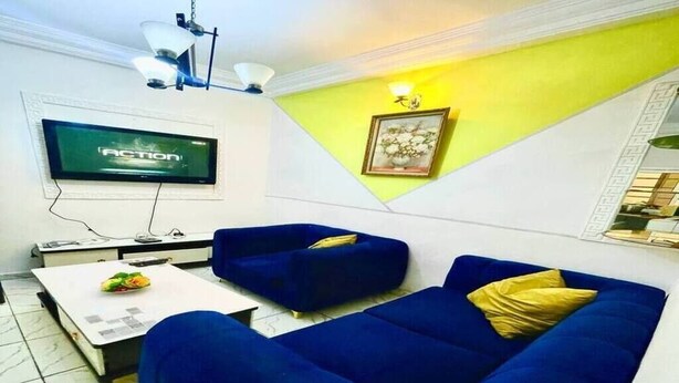 Un salon doté d’un téléviseur à écran plat, de deux canapés bleus avec des coussins jaunes, d’une table basse blanche et d’un mur d’accent jaune.