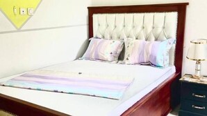 Un lit bien fait, doté d’une tête de lit capitonnée, une table de chevet avec une lampe et une prise de courant fixée au mur.