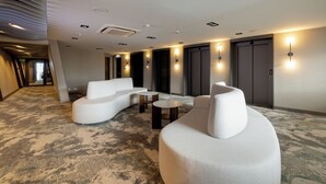 A modern hotel lobby with a curved white sofa, a round coffee table, and a carpeted floor.