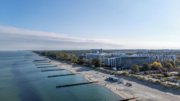 A coastal hotel with a long pier extending into the sea, modern buildings, and a clear view of the ocean.