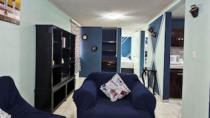 A living room with two blue sofas, a black entertainment unit, and a kitchen area in the background. - Departamento Centro Escolar (Tehuacán)
