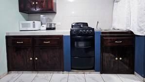 A compact kitchen with dark wooden cabinets, a white microwave, a black stove, and a sink. - Departamento Centro Escolar (Tehuacán)