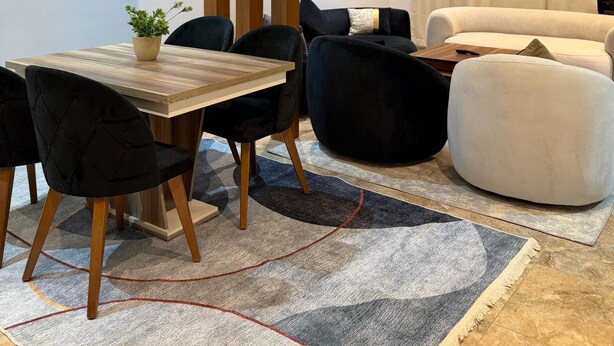 A modern living room with a dining area, featuring a wooden table, black upholstered chairs, a black sofa, and a white armchair. -  2-bedroom apartment with AC, WiFi in Casa Beverly Hills Compound-sheikh zayed (Giza Governorate)