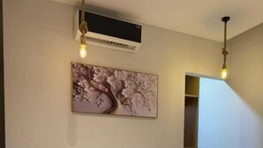 A bedroom with a bed, an air conditioning unit, a small bedside table, and a wall-mounted painting. -  2-bedroom apartment with AC, WiFi in Casa Beverly Hills Compound-sheikh zayed (Giza Governorate)