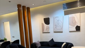 A modern living room with a black sofa, a wooden coffee table, and abstract wall art. -  2-bedroom apartment with AC, WiFi in Casa Beverly Hills Compound-sheikh zayed (Giza Governorate)
