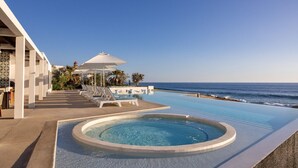 Un espace piscine doté d’un jacuzzi, de chaises longues et de parasols, avec vue sur l’océan.