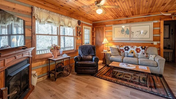 L’intérieur d’un chalet confortable, avec une cheminée, un fauteuil en cuir, un canapé et un ventilateur de plafond.