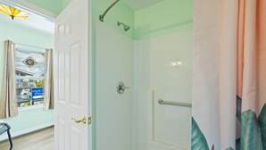 A bathroom with a shower, a toilet, and a sink. There is a window with curtains and a view of the outside. - Cozy Studio Retreat Above Cedar Key Island Bakery (Cedar Key)