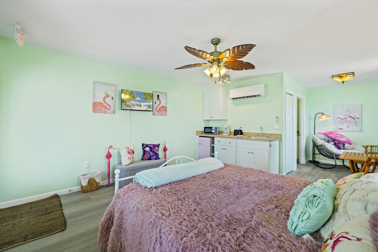 A bedroom with a bed, a ceiling fan, a kitchenette, and artwork on the walls.