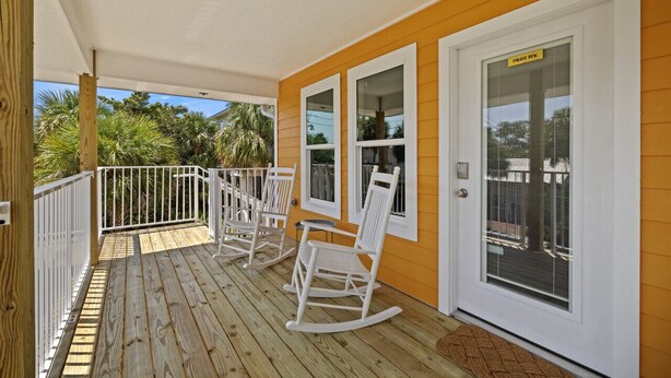 A wooden deck with white rocking chairs and a white door with a peephole. - Cozy Studio Retreat Above Cedar Key Island Bakery (Cedar Key)