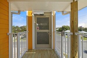A covered porch with a white door and a glass panel, surrounded by a white railing, leading to a driveway. - The Pirate`s Den Above Cedar Key Island Bakery (Cedar Key)