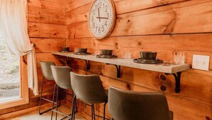Interior de madera con una mesa larga, cuatro sillas y un reloj de pared.