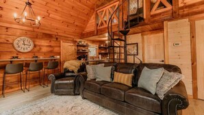 Interior acogedor de una cabaña con detalles de madera, un sofá de cuero, un comedor y una escalera.