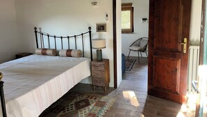 Une chambre à coucher comprenant un lit, une table de chevet, une lampe et une porte en bois donnant sur une autre pièce.